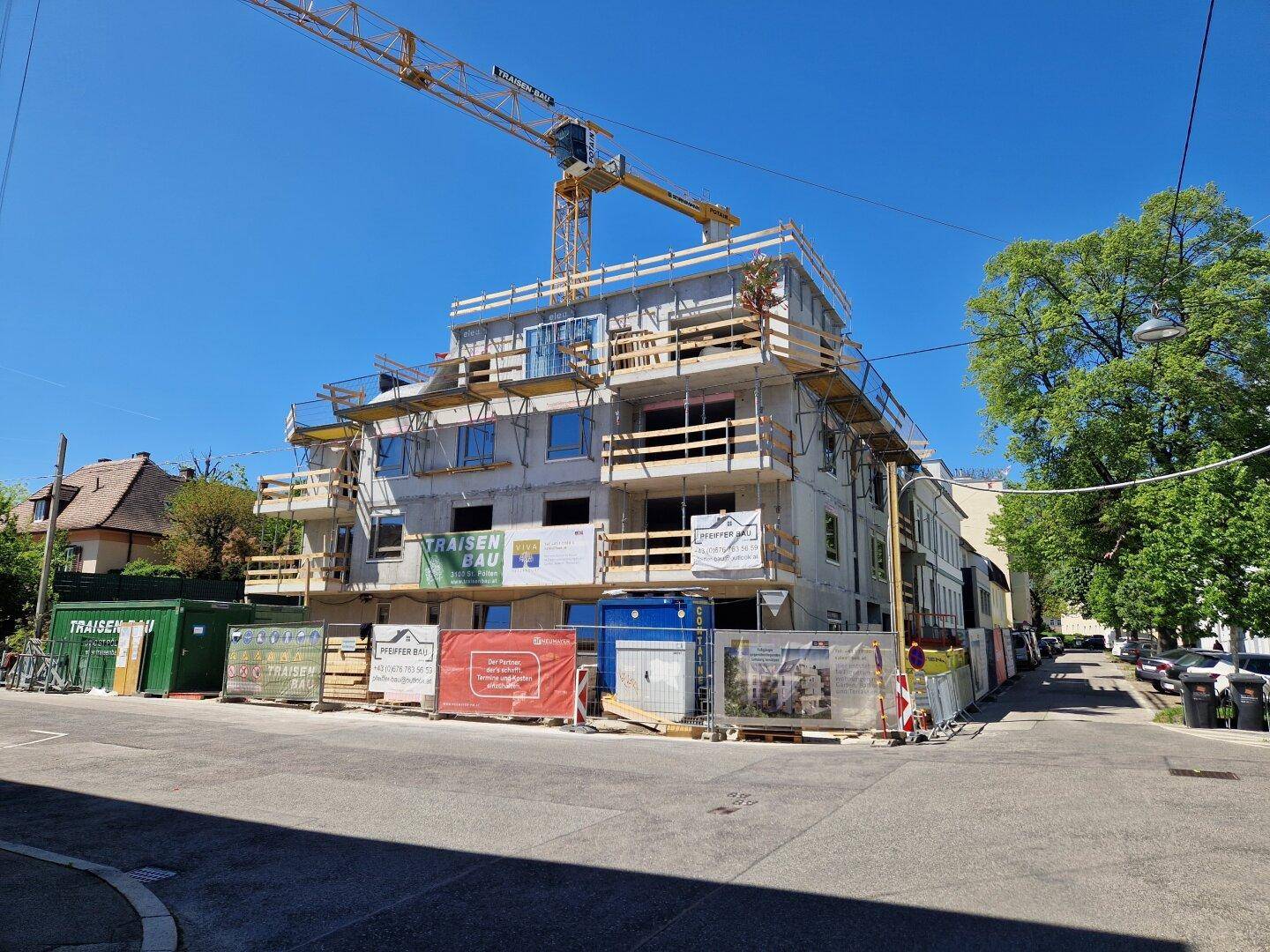 Baustelle eines Mehrfamilienhauses mit Gerüst und Baukränen unter strahlend blauem Himmel.