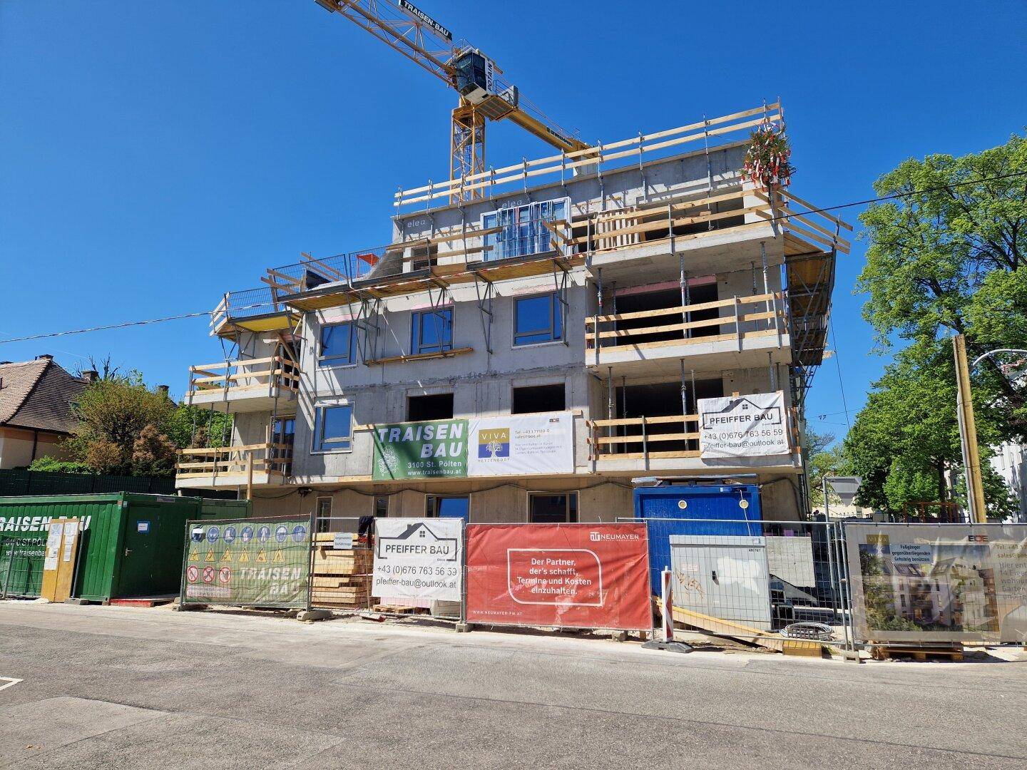 Frontansicht der Baustelle eines Neubaus mit Baukränen und Werbebannern.