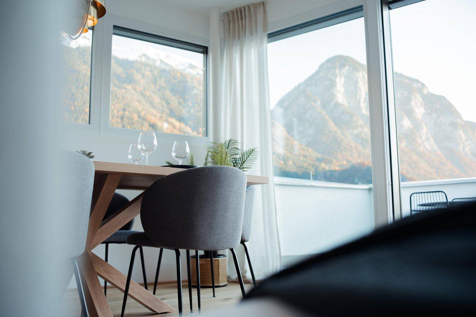 Eleganter Essbereich mit modernem Holztisch und Stühlen, umgeben von großen Fenstern mit beeindruckendem Bergblick.