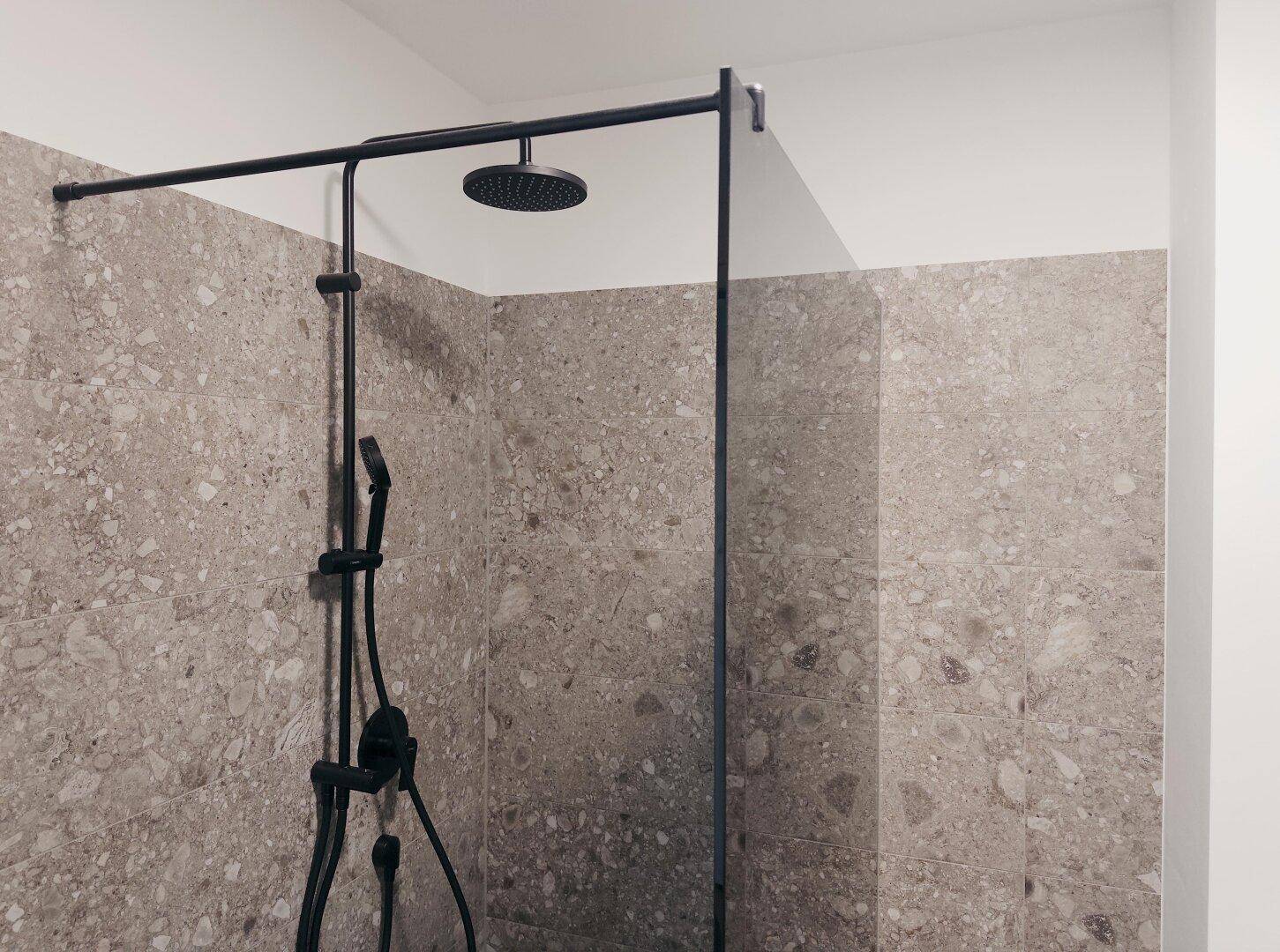 Detailansicht der modernen begehbaren Dusche mit dunklen Armaturen und großformatigen Fliesen.