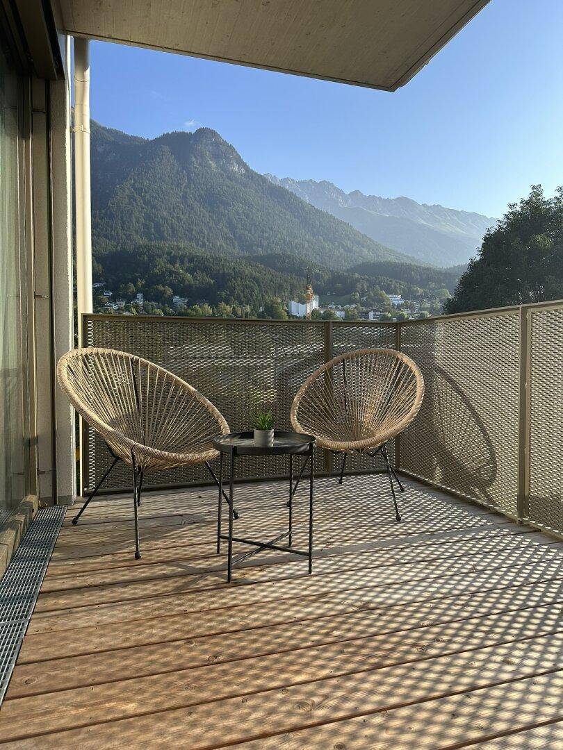 Kleiner Balkon mit Holzboden, Sitzgelegenheiten und malerischem Bergblick in der Sonne.