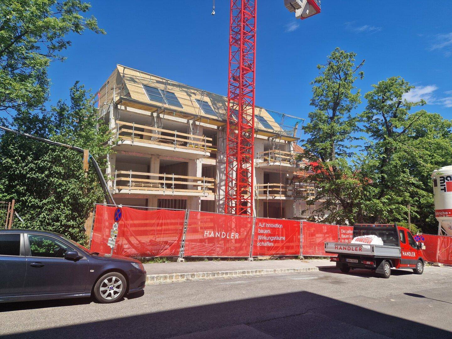 Neubau im Rohbauzustand mit Baugerüst und Kran unter blauem Himmel.