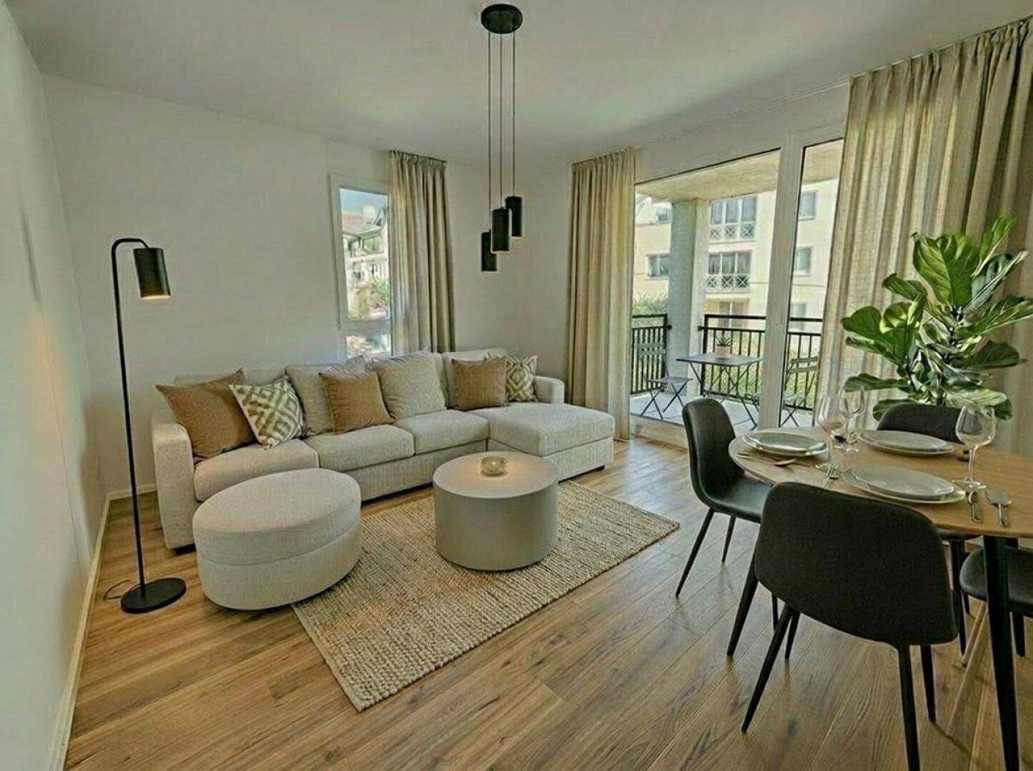 Heller Wohn- und Essbereich mit modernem Sofa, Holzboden und Zugang zu einem Balkon.