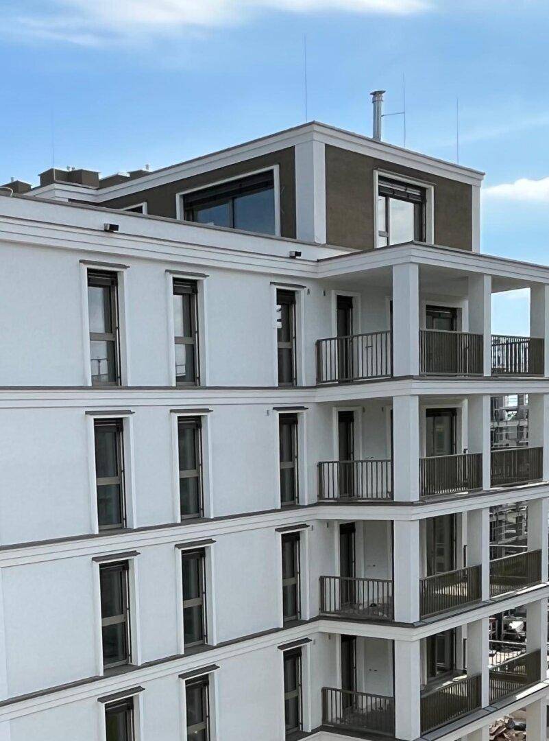 Modernes Gebäude mit gestaffelten Balkonen und markantem Dachgeschoss unter blauem Himmel.
