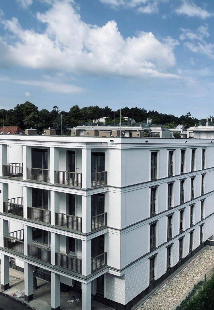 Moderne Wohnanlage mit weißer Fassade, vielen Balkonen und Blick auf grüne Bäume unter blauem Himmel.
