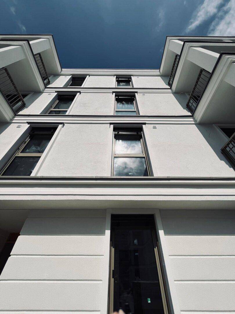 Vertikale Ansicht der weißen Fassade eines modernen Wohngebäudes mit zahlreichen Fenstern und Balkonen.