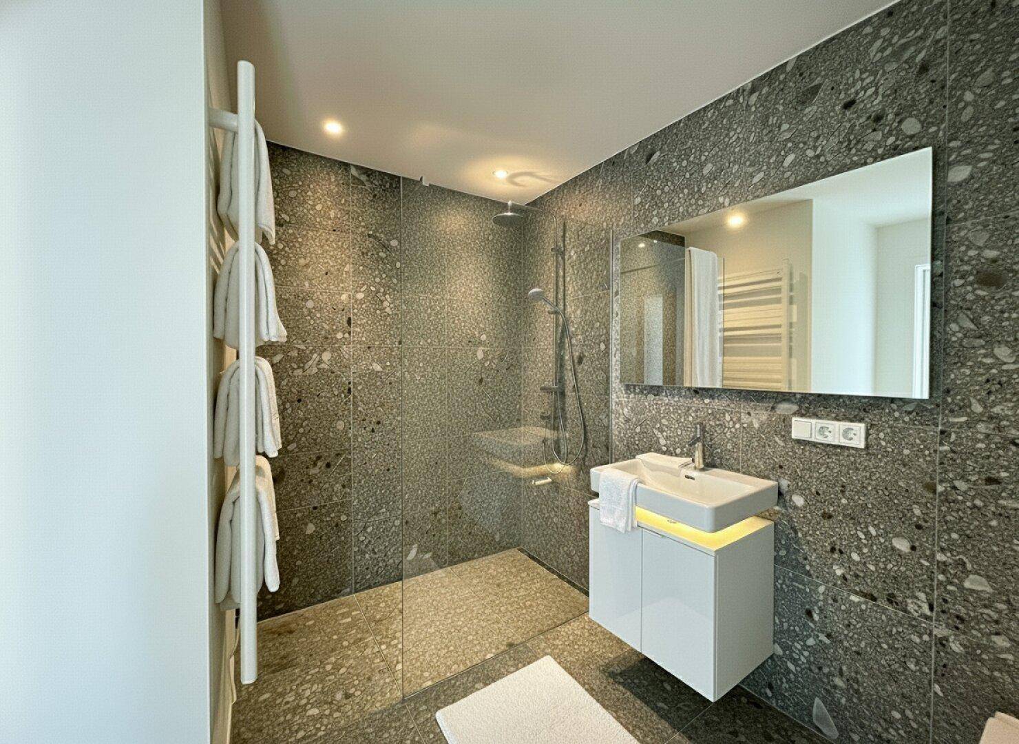 Modernes Badezimmer mit großformatigen grauen Fliesen, begehbarer Dusche und Einzelwaschbecken.
