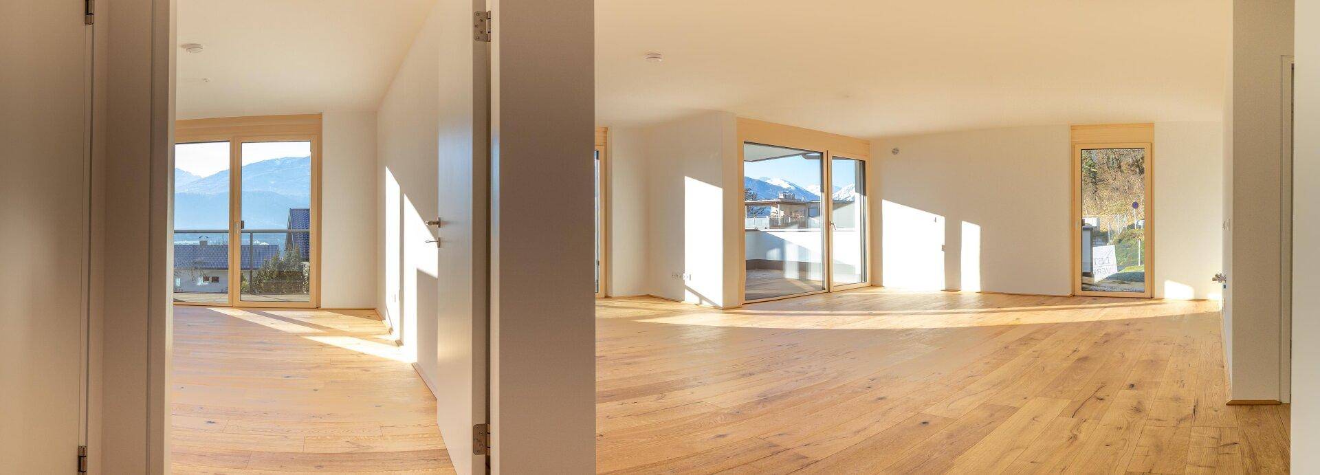 Helle, leere Räume mit Holzboden, großen Fenstern und Bergblick.