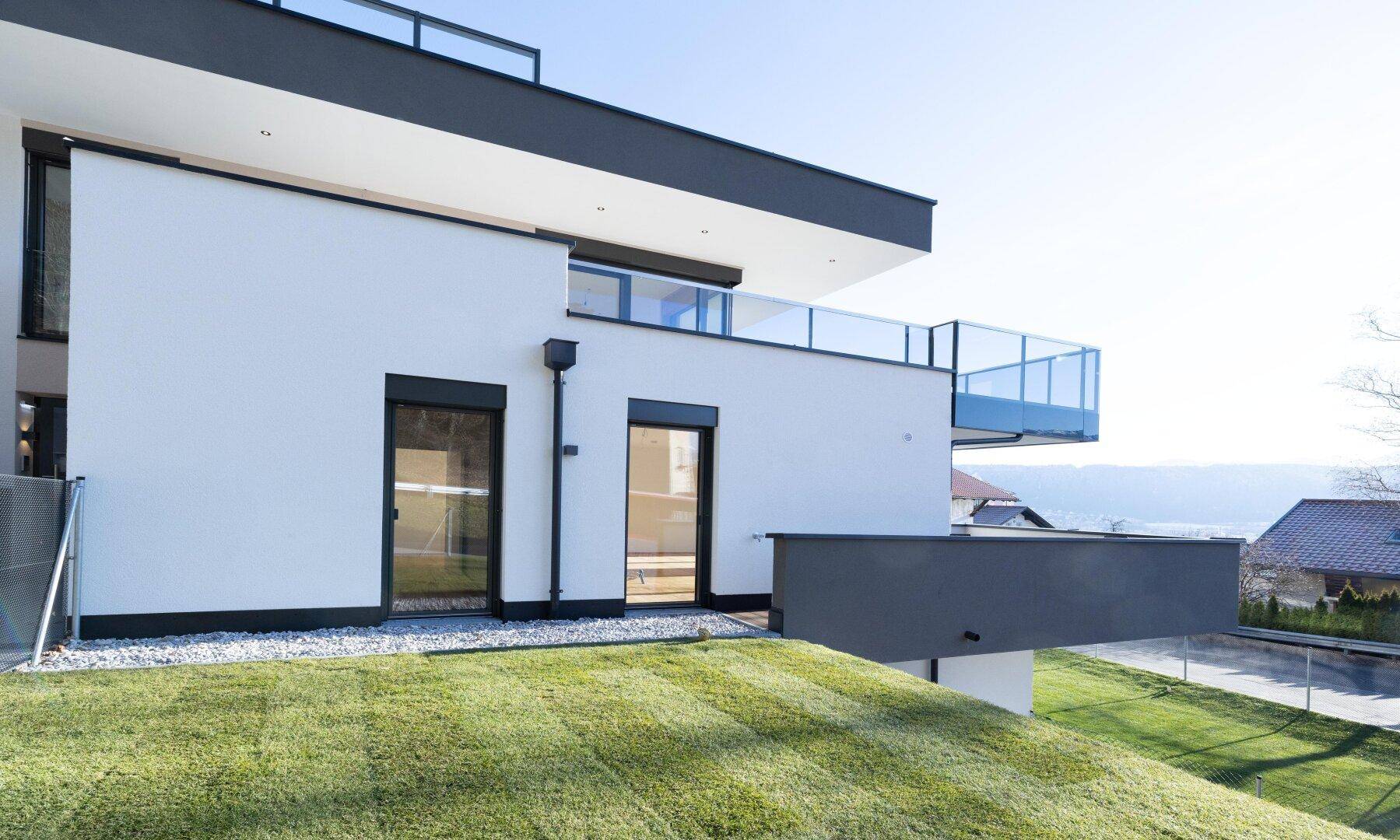 Moderne Gebäudefassade mit Balkon, Gartenbereich und Blick auf den See.