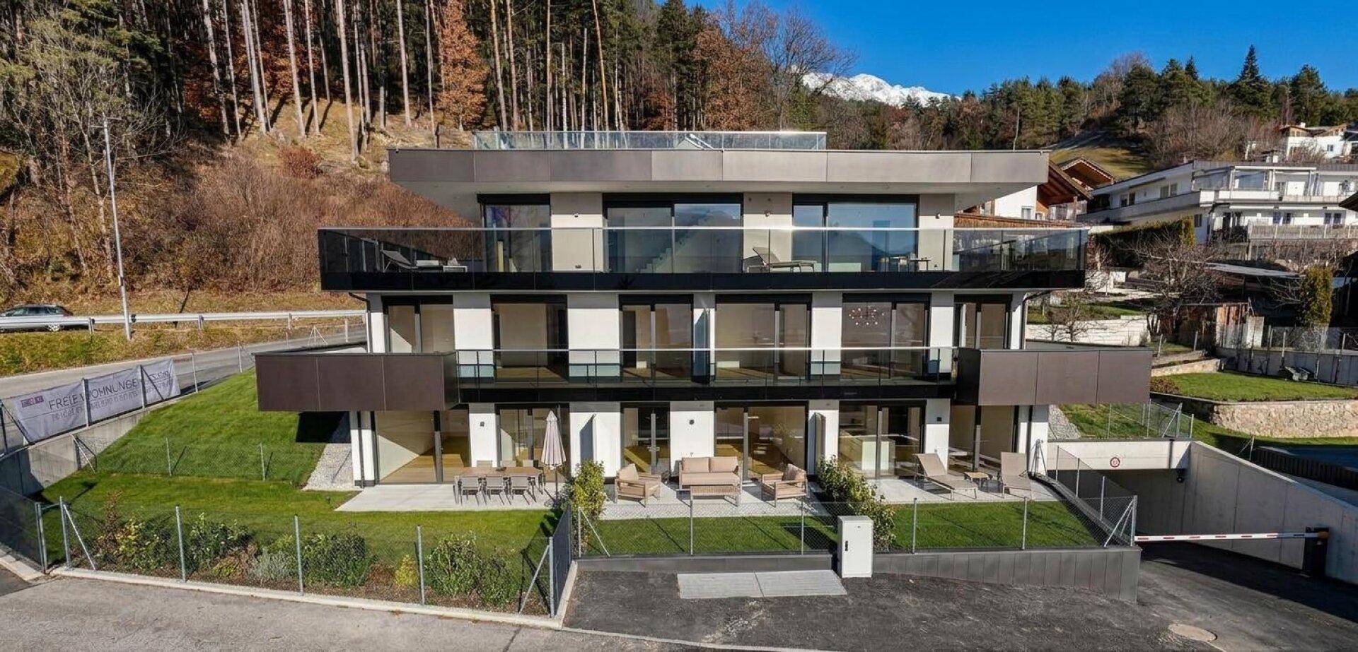 Modernes Mehrfamilienhaus mit mehreren Balkonen, Tiefgarage und Bergblick.