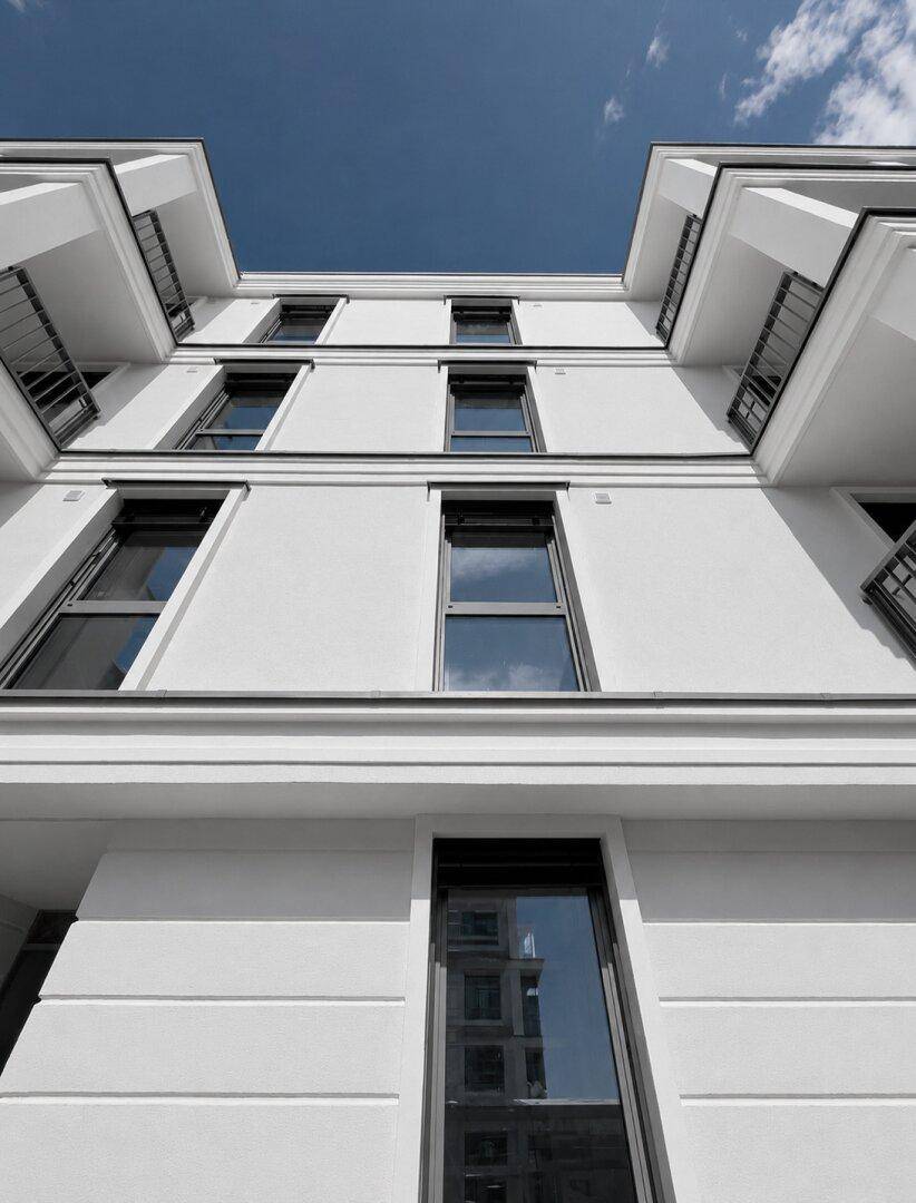 Nahaufnahme einer modernen, weißen Gebäudefassade mit großen Fenstern und Balkonen unter blauem Himmel.