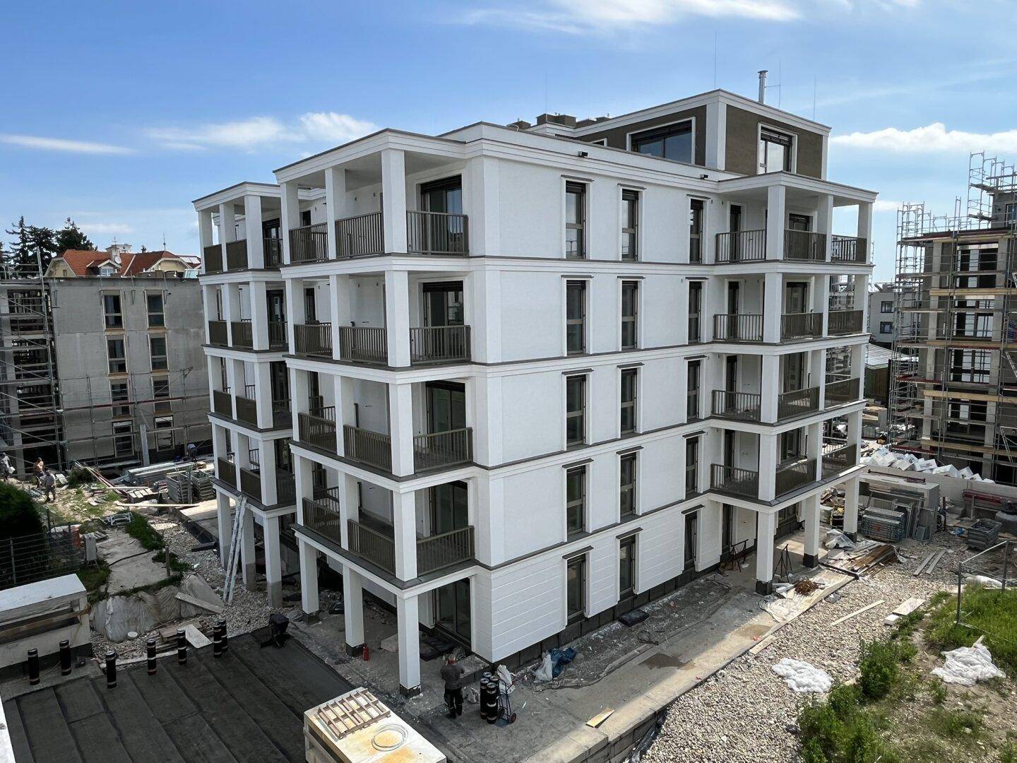 Neubau eines modernen Wohngebäudes mit Balkonen, umgeben von weiteren Baustellen in Entwicklung.