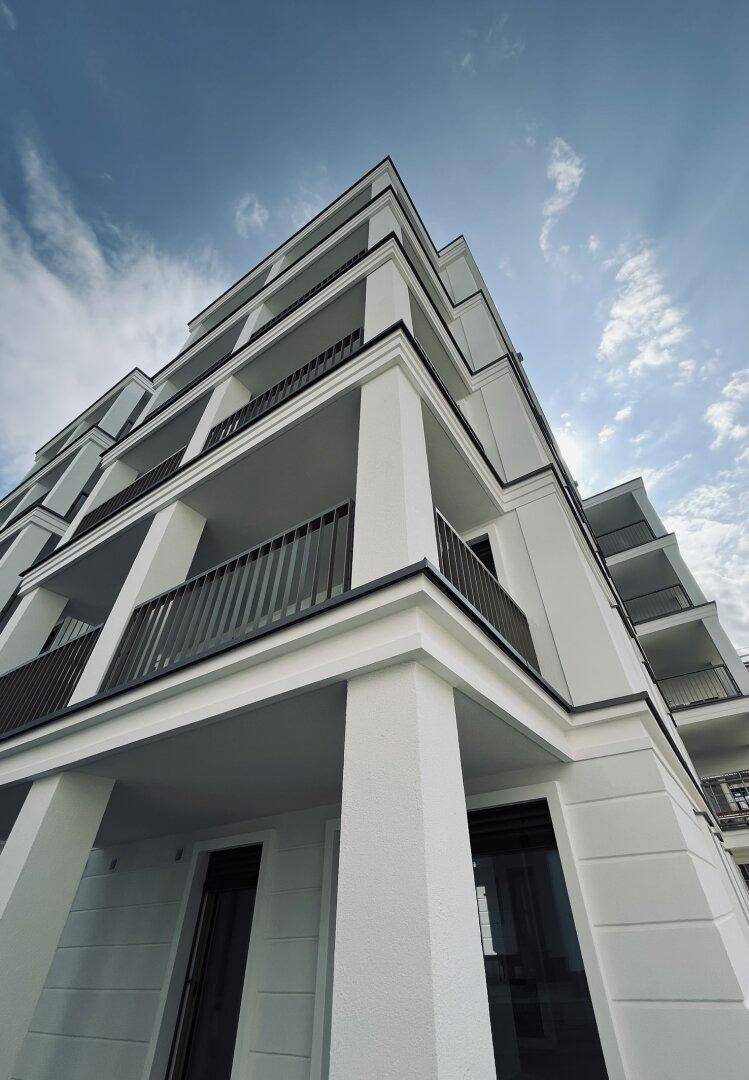 Architektonische Ansicht eines modernen Wohngebäudes mit klaren Linien und Balkonen unter weitem Himmel.