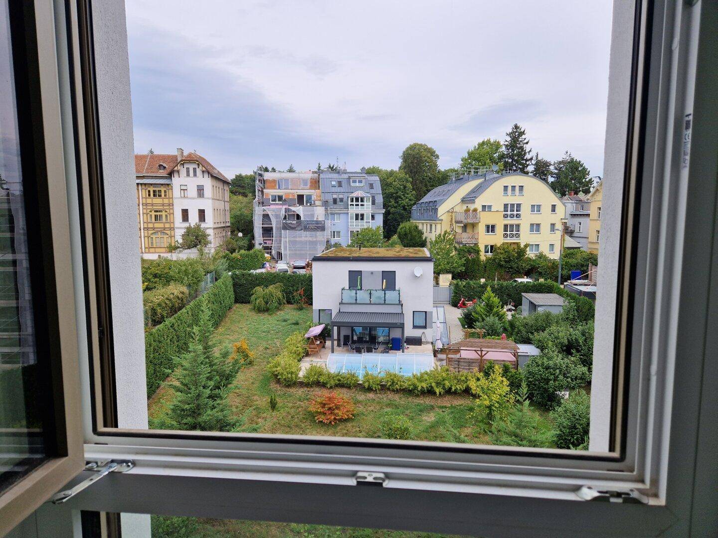 Blick aus einem Fenster auf eine Wohngegend mit Häusern, Gärten und einem Pool.