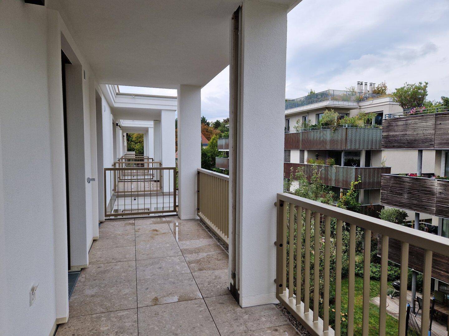 Lange, überdachte Loggia mit Fliesenboden und Blick auf die umliegenden Gärten und Gebäude.