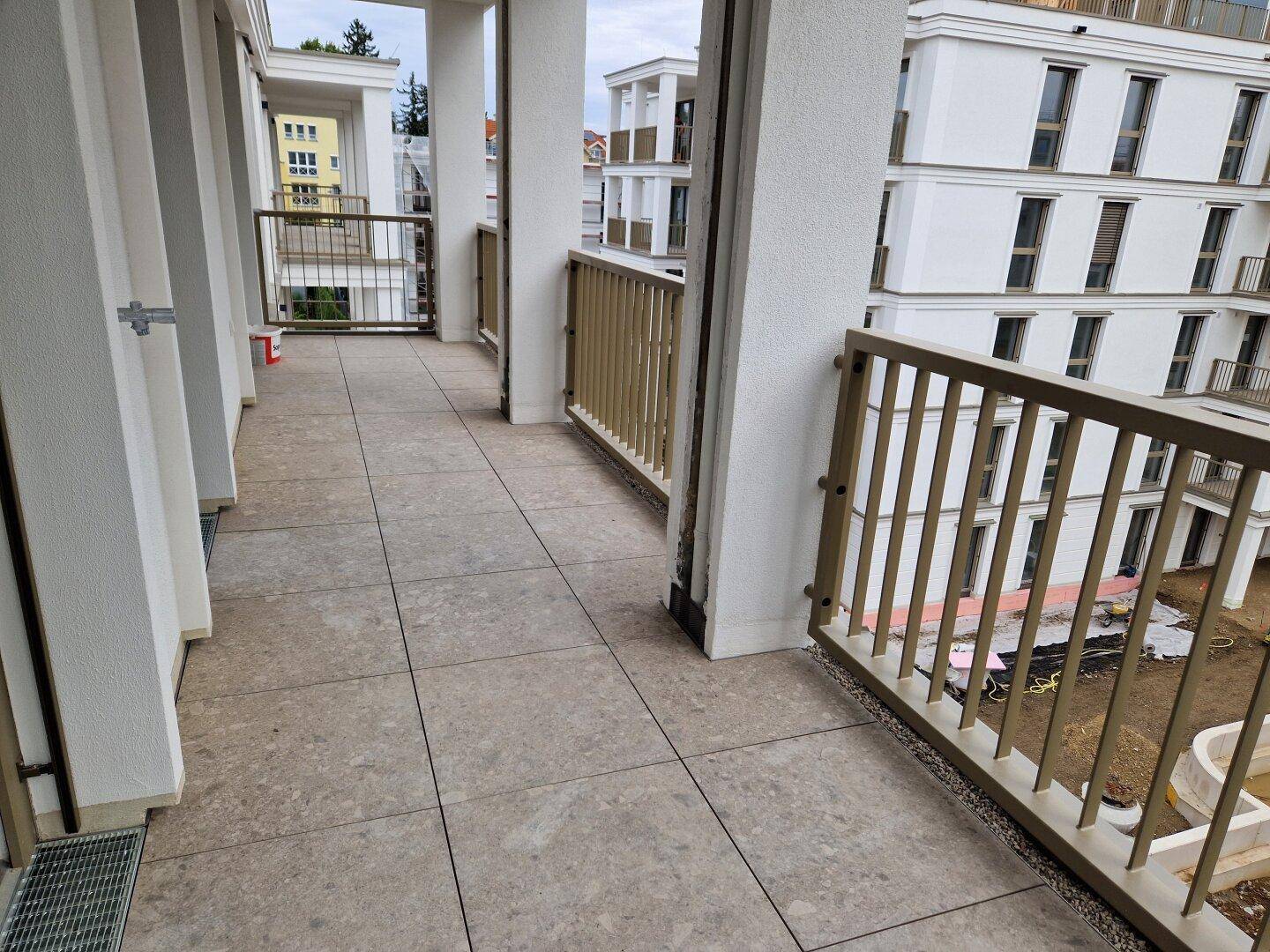 Langer, gefliester Balkon mit modernen Metallgeländern und Blick auf die umliegenden Neubauten.