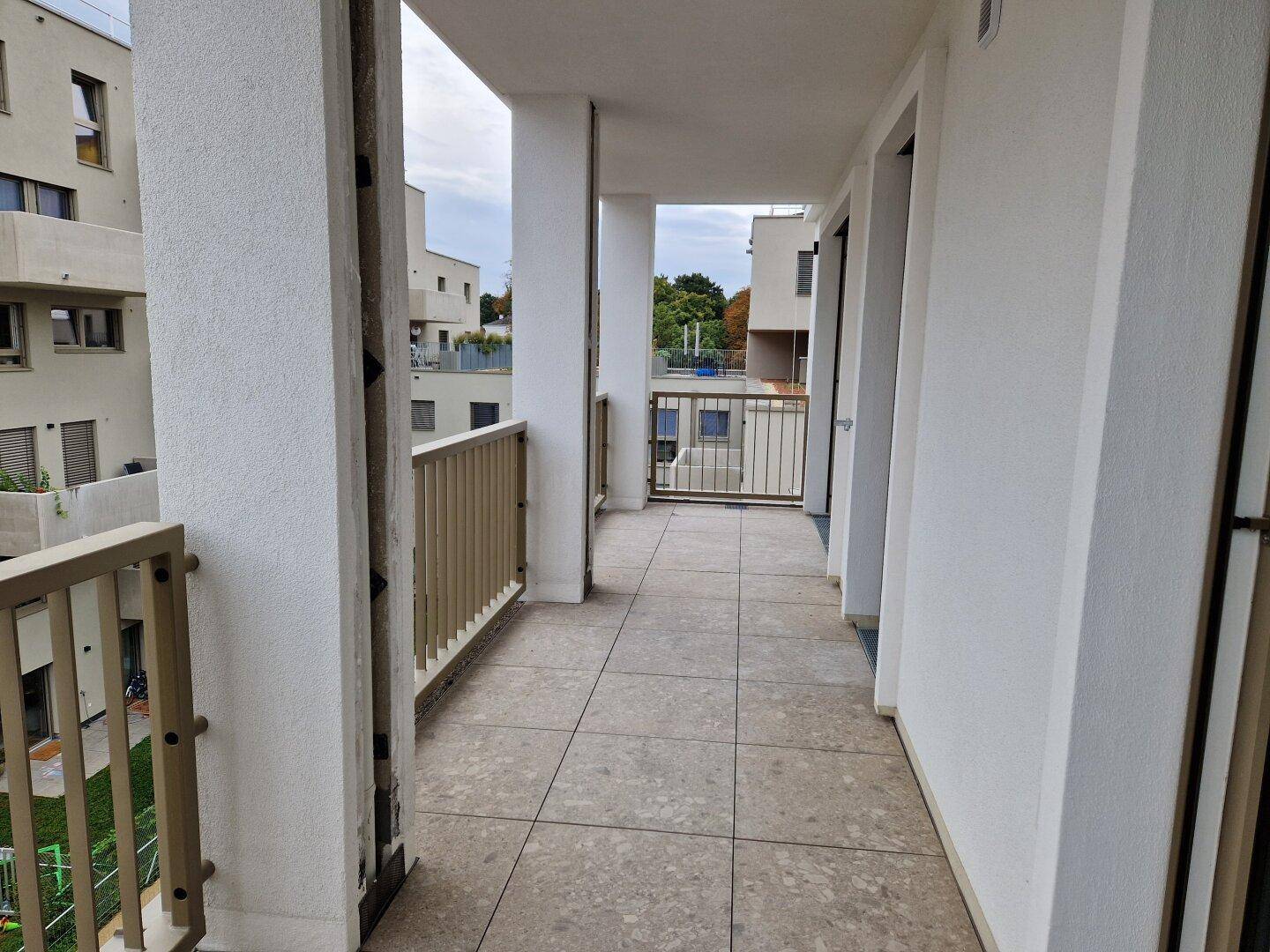 Geräumiger Balkon mit Fliesenboden und Blick auf die moderne Wohnanlage und Grünflächen.