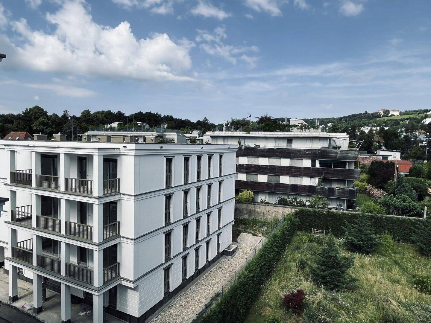Modernes Mehrfamilienhaus mit weißer Fassade, mehreren Loggien und weitem Blick ins Grüne.