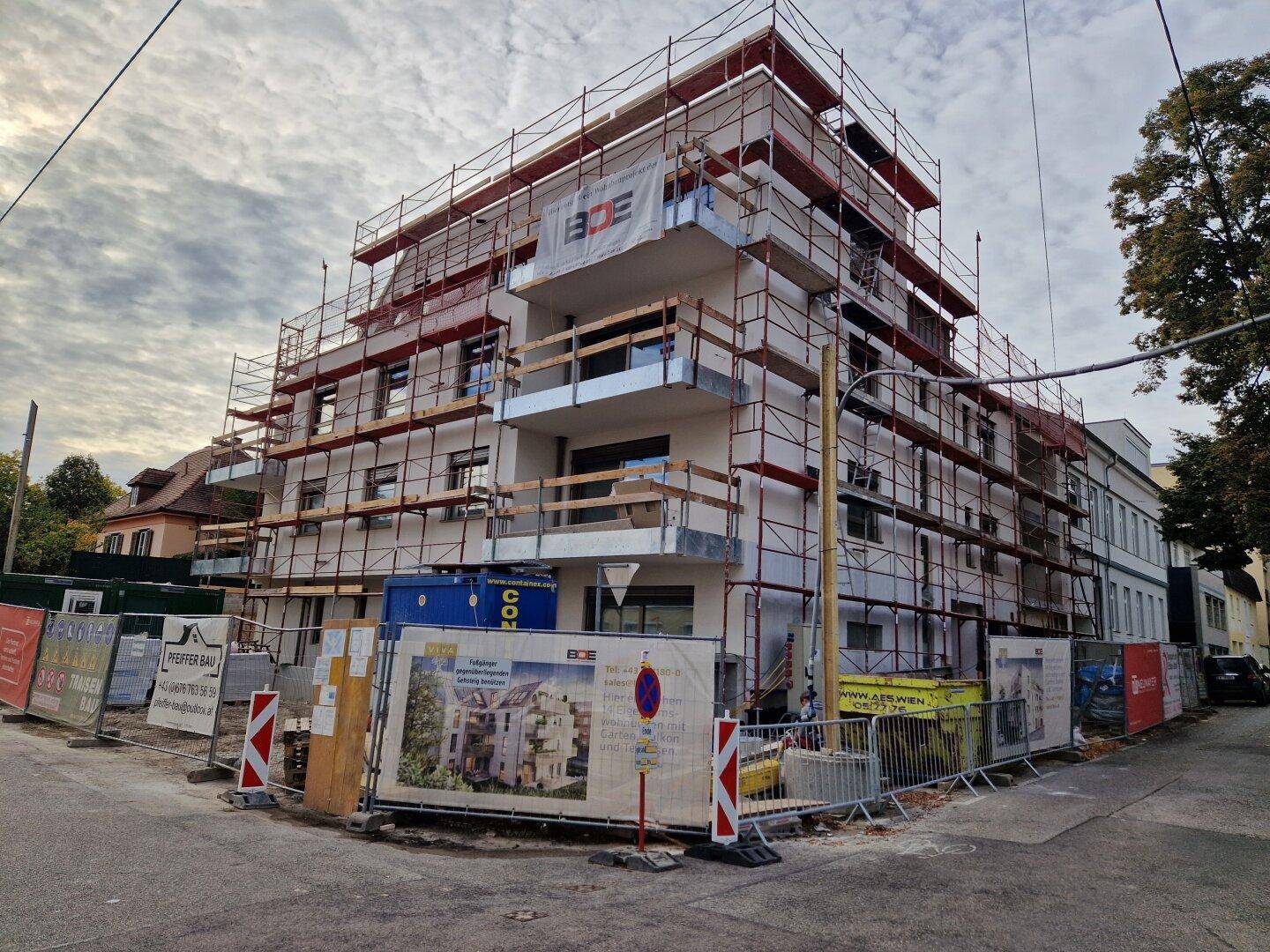 Neubaugebäude mit Gerüst und Baustellenschildern unter bewölktem Himmel, bereit zur Fertigstellung.