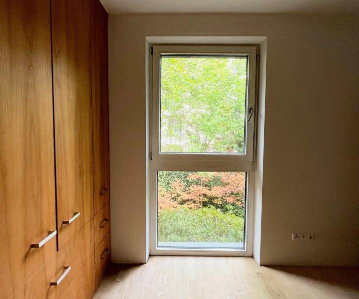 Schlafzimmer mit Einbauschränken, Holzboden und Fenster mit Blick ins Grüne.