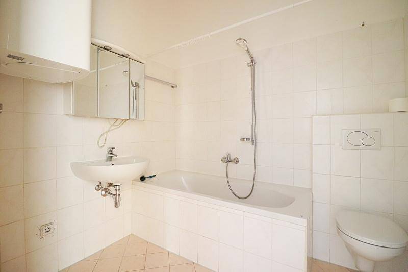 Helles Badezimmer mit weißen Fliesen, Badewanne mit Duschfunktion, wandhängendem WC und Waschbecken mit Spiegelschrank.