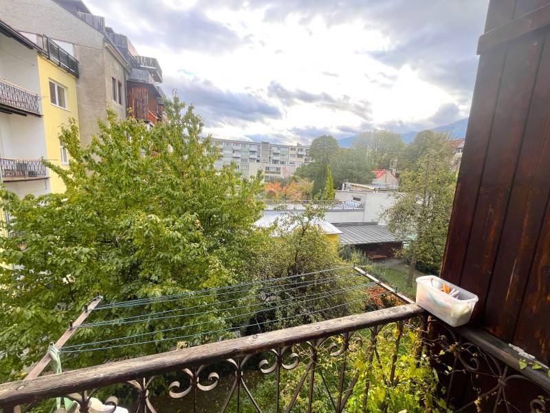 Ausblick von einem Balkon mit Blick auf grüne Bäume und umliegende Gebäude unter einem bewölkten Himmel.