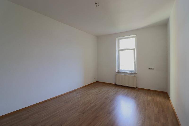 Leeres Zimmer mit hellem Holzfußboden und einem Fenster, das viel Tageslicht hereinlässt.