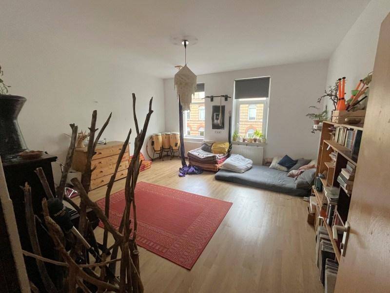Gemütlicher Wohnbereich mit Holzboden, rotem Teppich und individueller Einrichtung, inklusive Bücherregal und Sitzgelegenheiten.