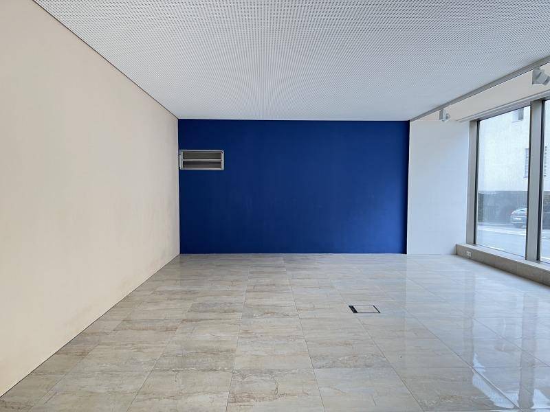 Leerer Gewerberaum mit blauer Akzentwand, beigen Wänden und glänzenden Fliesenböden.