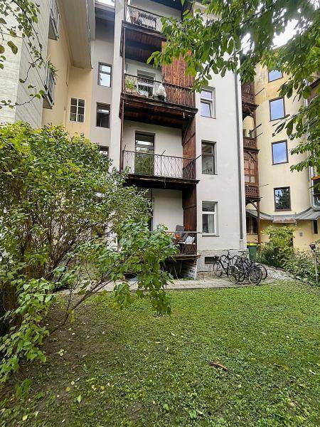 Rückansicht eines Gebäudes mit mehreren Balkonen, umgeben von einem grünen Gartenbereich und Bäumen.