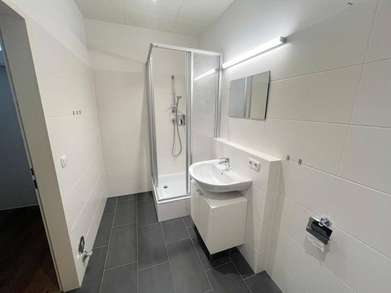 Modern gefliestes Badezimmer mit Duschkabine, Waschtisch und Wand-WC.