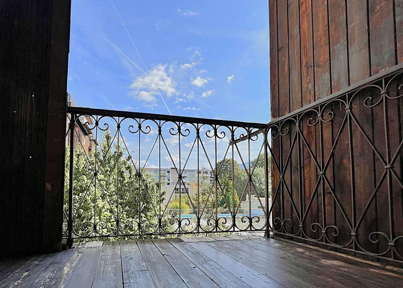 Leerer Balkon mit schmiedeeisernem Geländer und Holzboden, bietet einen weiten Blick auf die Umgebung.