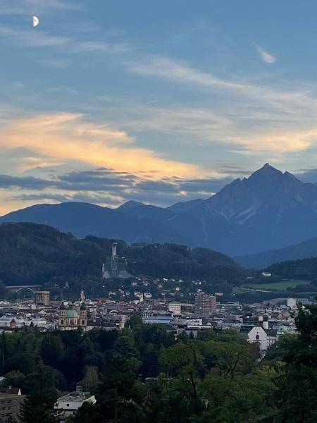 Panoramablick auf eine Stadt mit Bergen im Hintergrund unter einem bewölkten Himmel.