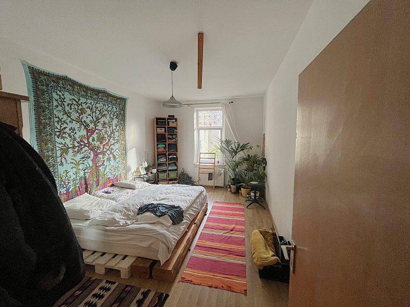 Schlafzimmer mit kreativem Palettenbett, farbenfrohem Wandteppich und vielen Pflanzen, die eine entspannte Atmosphäre schaffen.