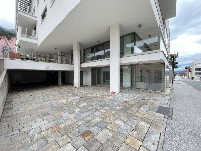 Eingangsbereich eines modernen Gebäudes mit gepflastertem Vorplatz und Zugang zur Tiefgarage.