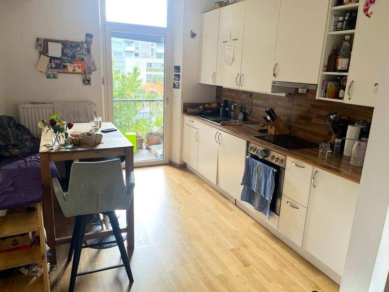 Funktionale Küchenzeile mit weißen Schränken, Holzarbeitsplatte und Essbereich, mit Zugang zu einem Balkon.