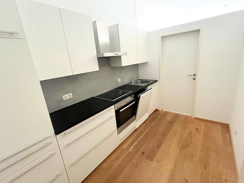 Moderne Einbauküche mit weißen Schränken, dunkler Arbeitsplatte und integrierten Geräten.