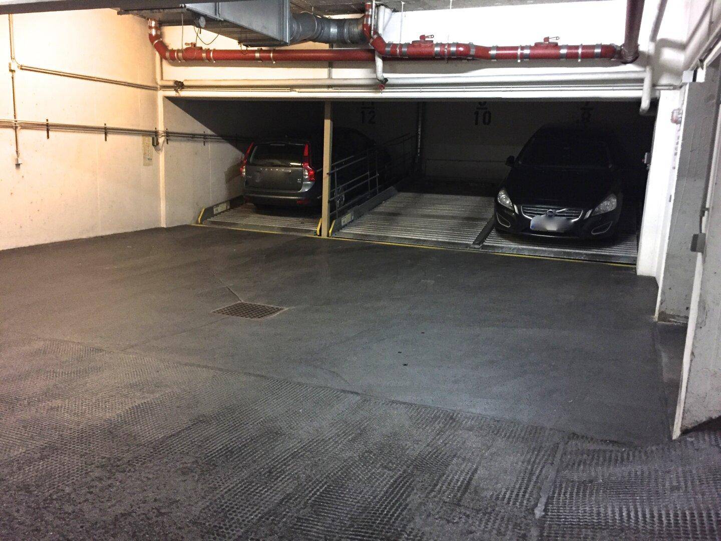 Zwei Fahrzeuge parken auf einem automatischen Parksystem in einer Tiefgarage mit sichtbaren Rohren.