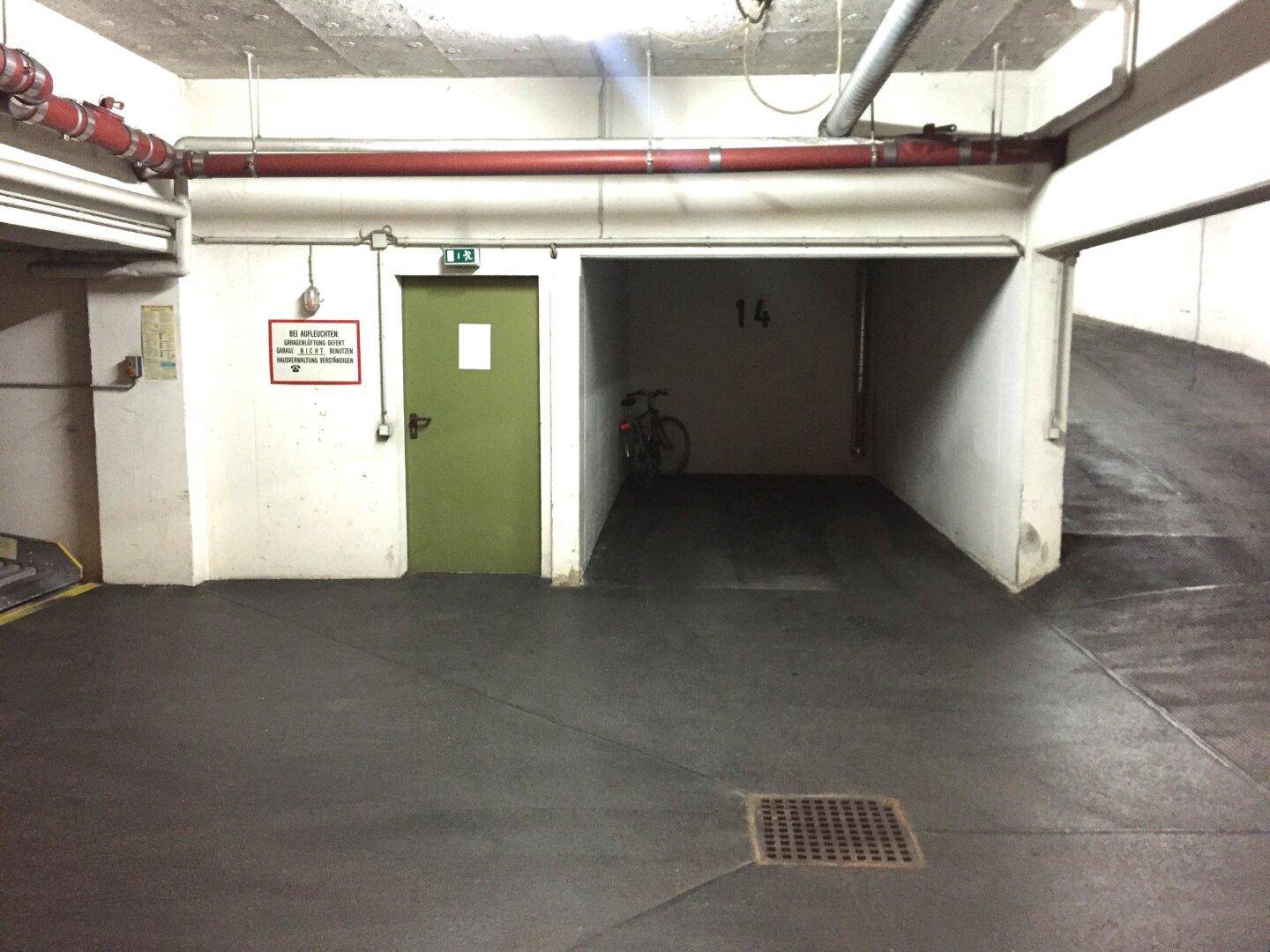 Leerer Stellplatz Nummer 14 in einer Tiefgarage mit einem Fahrrad und einer grünen Tür.