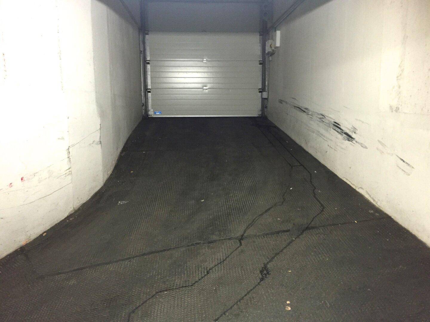 Einzelne Garagenbox in einer Tiefgarage mit geschlossenem Rolltor und Abnutzungsspuren an den Wänden.