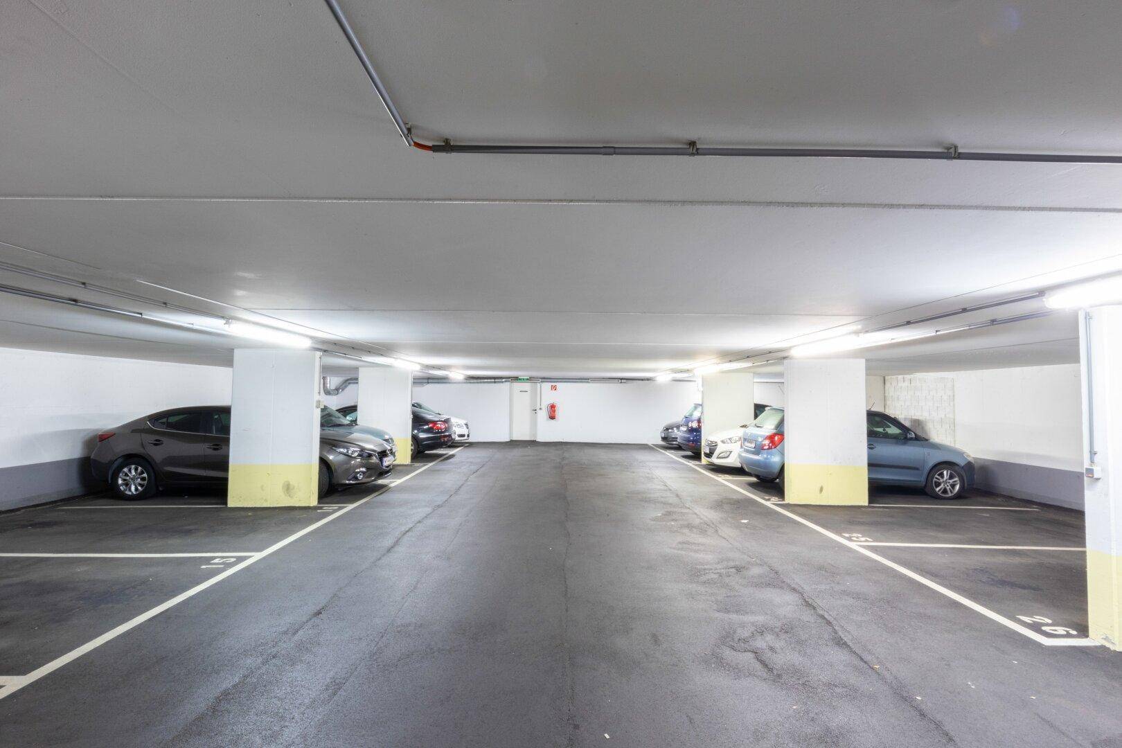 Geräumige Tiefgarage mit mehreren geparkten Fahrzeugen und hellen Leuchtstoffröhren.