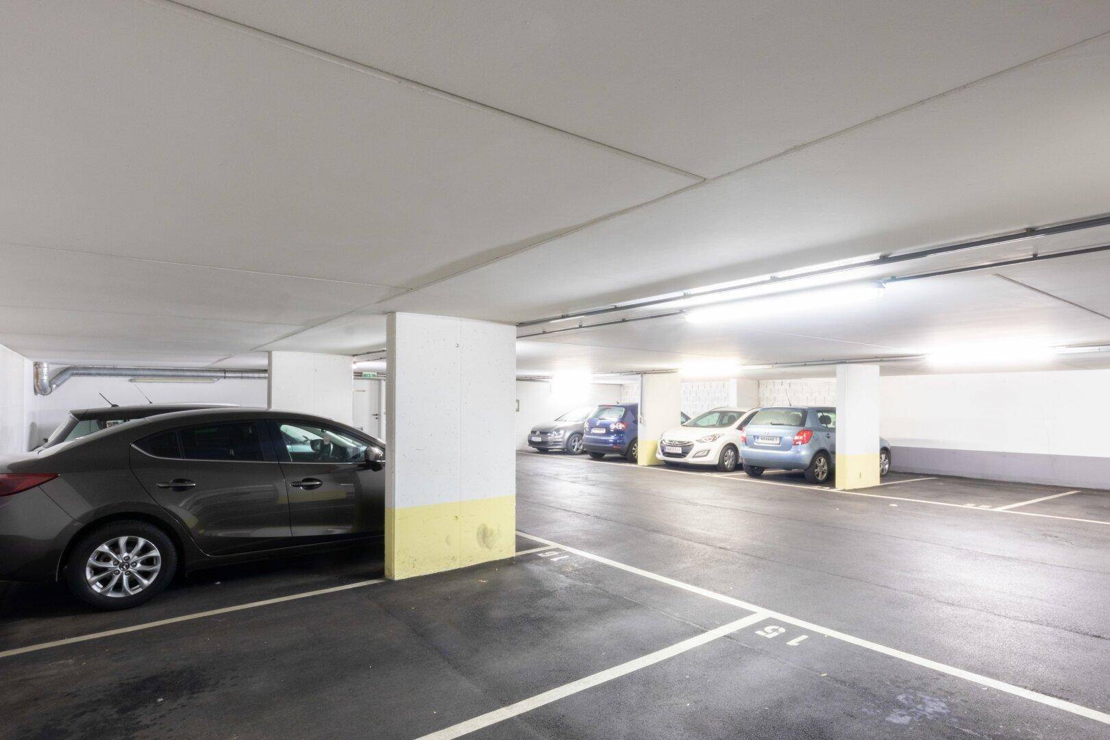 Saubere und gut beleuchtete Tiefgarage mit markierten Parkplätzen und Säulen.