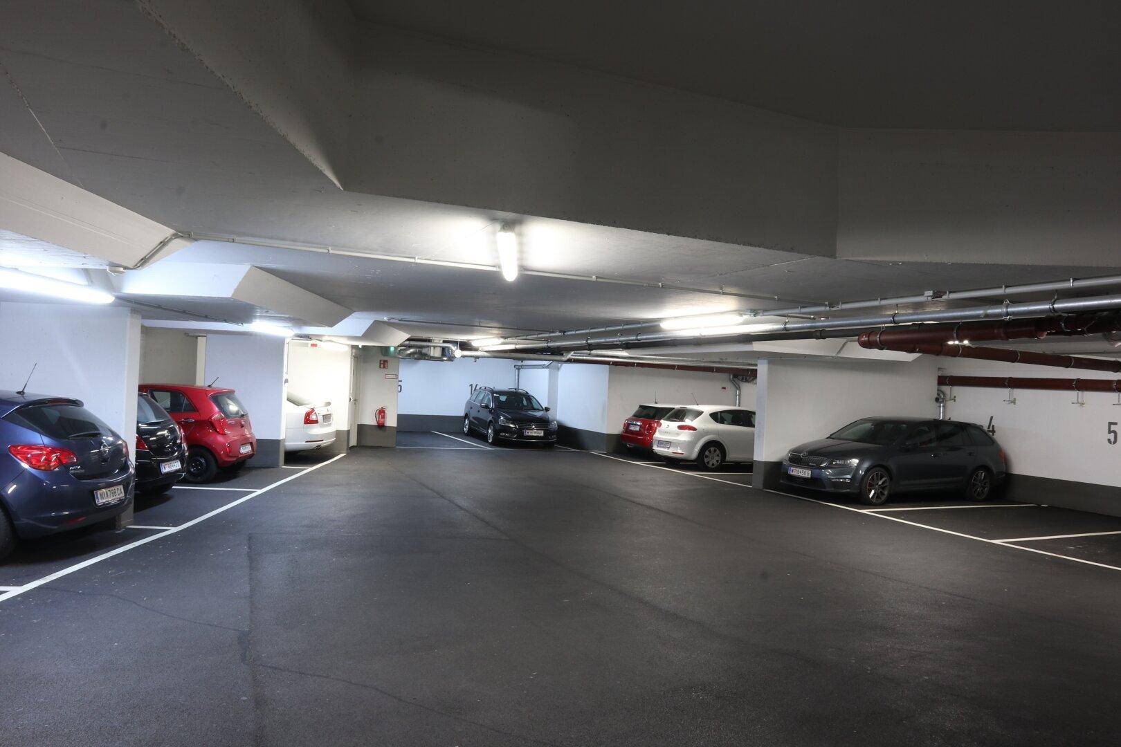 Tiefgarage mit mehreren geparkten Autos, Betonwänden und Decken sowie heller Beleuchtung.