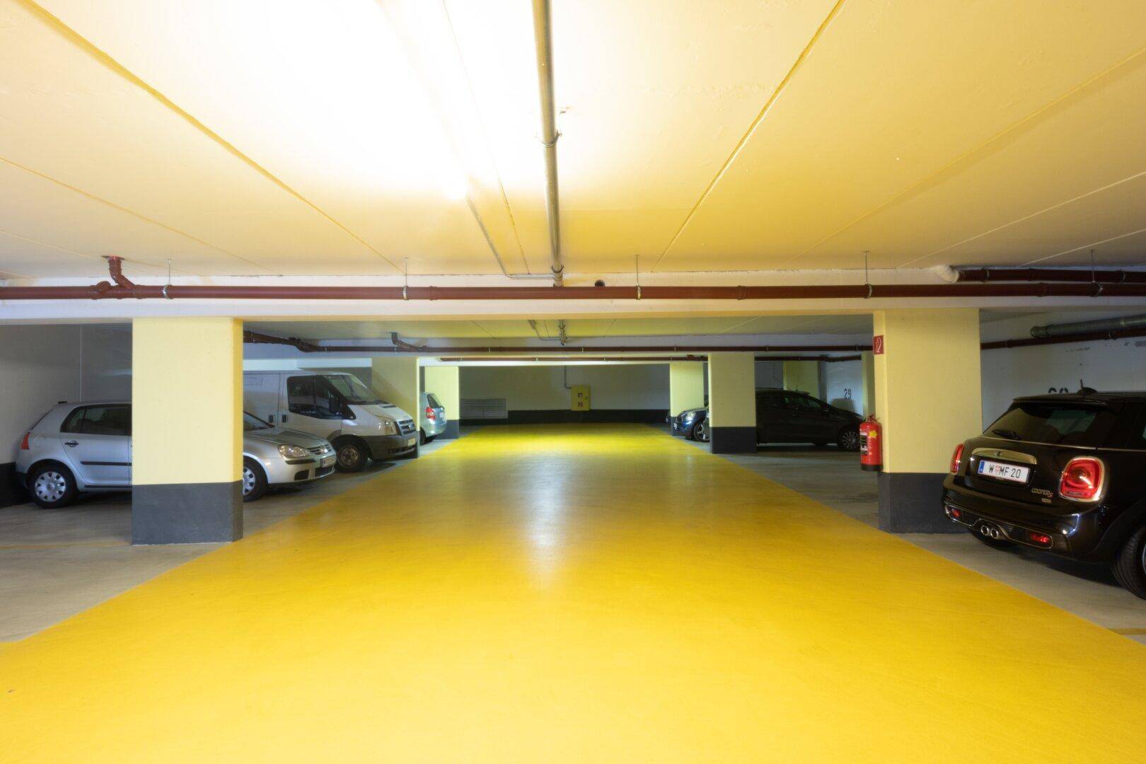 Helle Tiefgarage mit gelbem Boden, vielen Parkplätzen und funktionaler Beleuchtung.