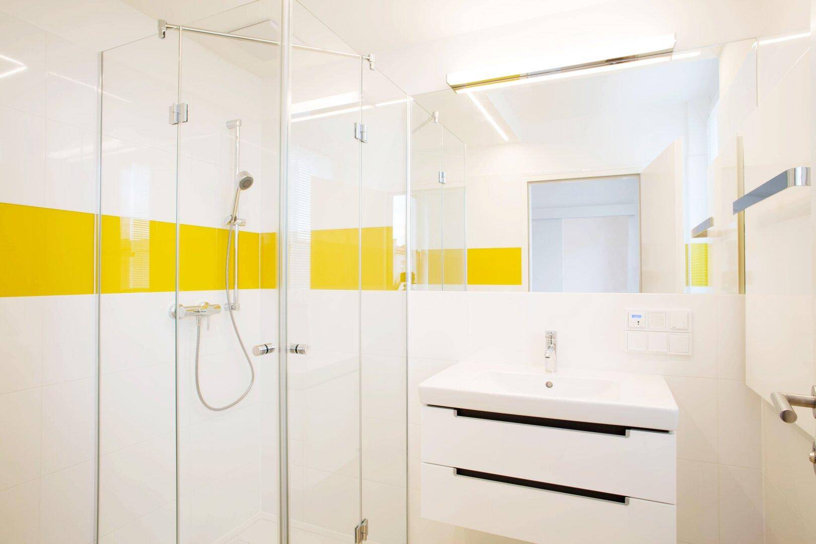 Modernes Badezimmer mit gelben Akzentfliesen, Glasdusche und stilvollem Waschtisch.