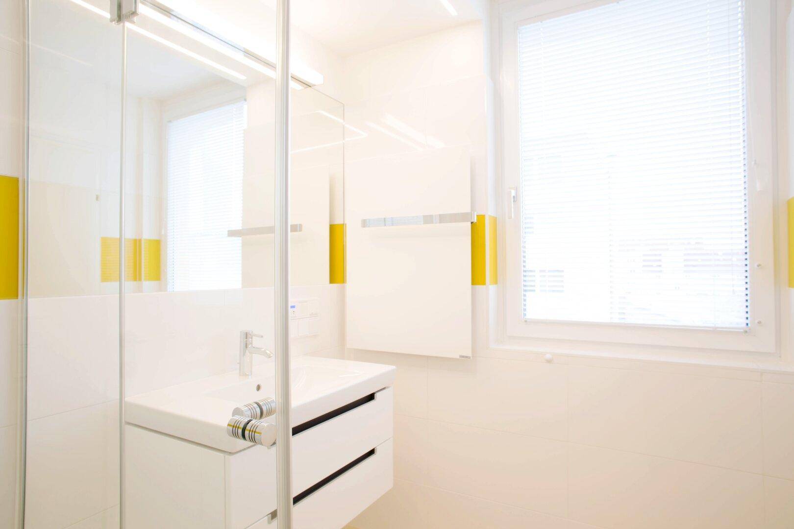 Helles Badezimmer mit Fenster, gelben Akzenten, moderner Dusche und Waschtisch.