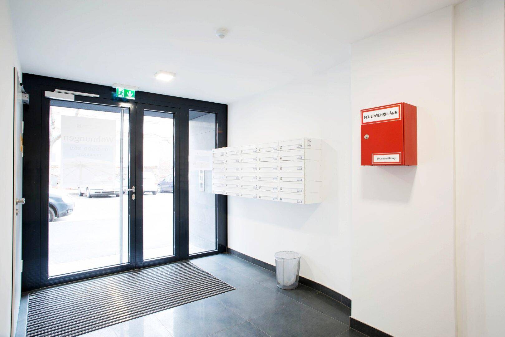 Heller Eingangsbereich mit Glasportal, Briefkästen und Brandschutzinformationen.