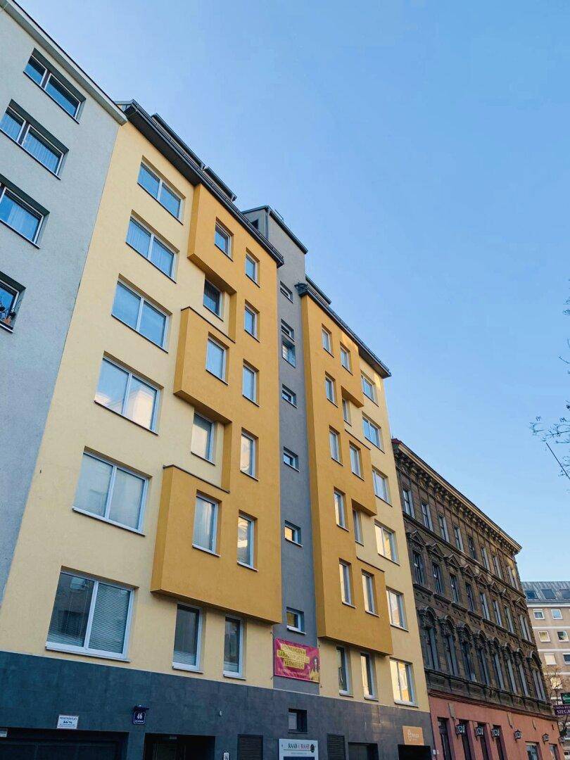 Moderne Gebäudefassade mit gelben und grauen Farbakzenten und vielen Fenstern.