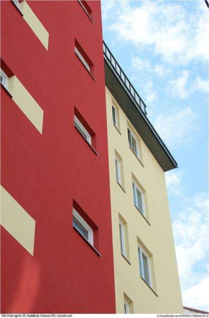 Moderne Gebäudefassade mit roten und beigen Akzenten unter blauem Himmel.