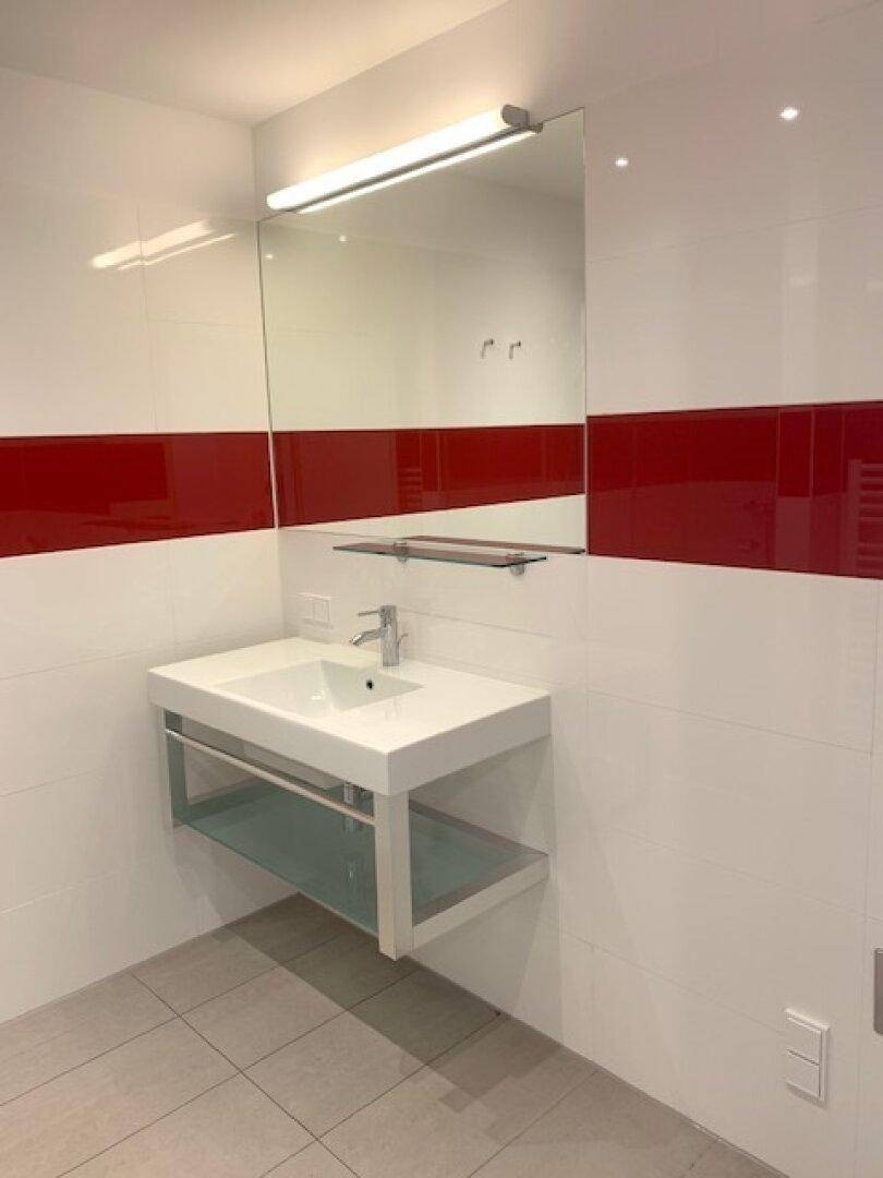 Modernes Badezimmer mit weiß-roten Fliesen, Einzelwaschbecken und großem Spiegel.